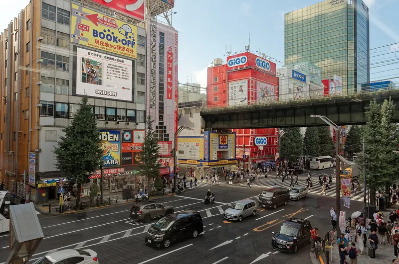 A street junction in Akihabara with electronics and game-arcade signs and a railway bridge