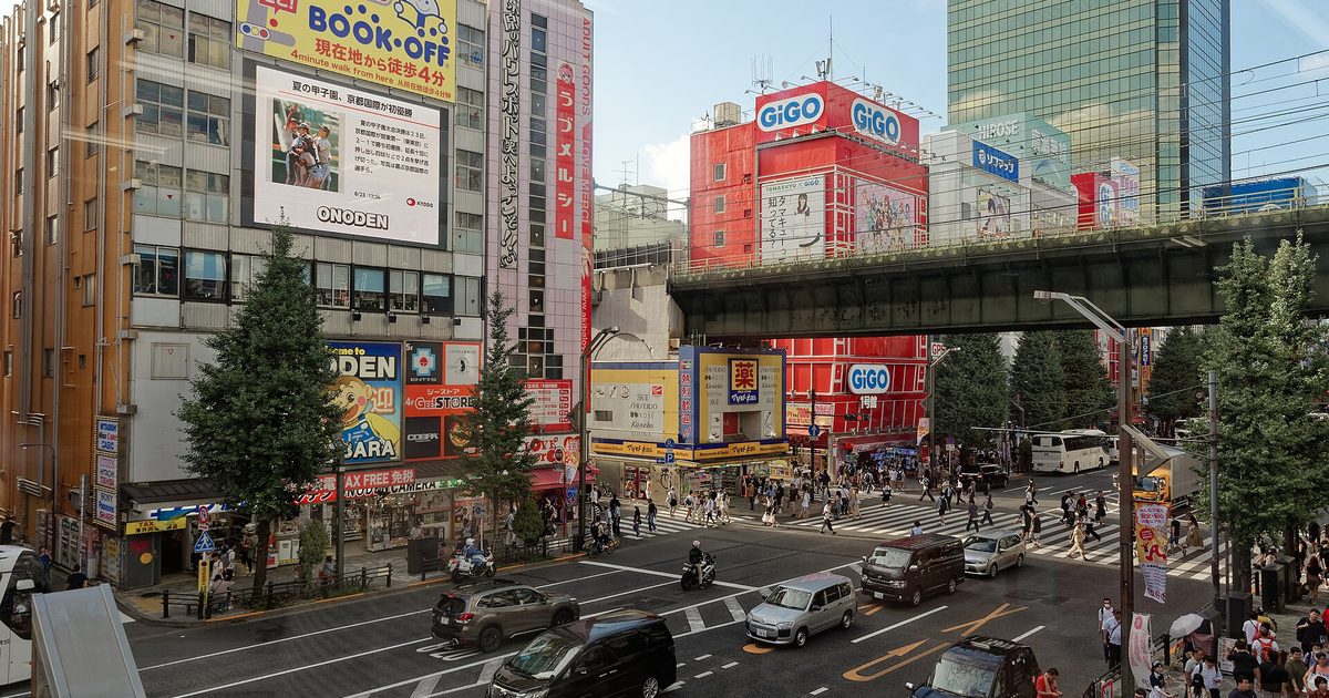 A street junction in Akihabara with electronics and game-arcade signs and a railway bridge