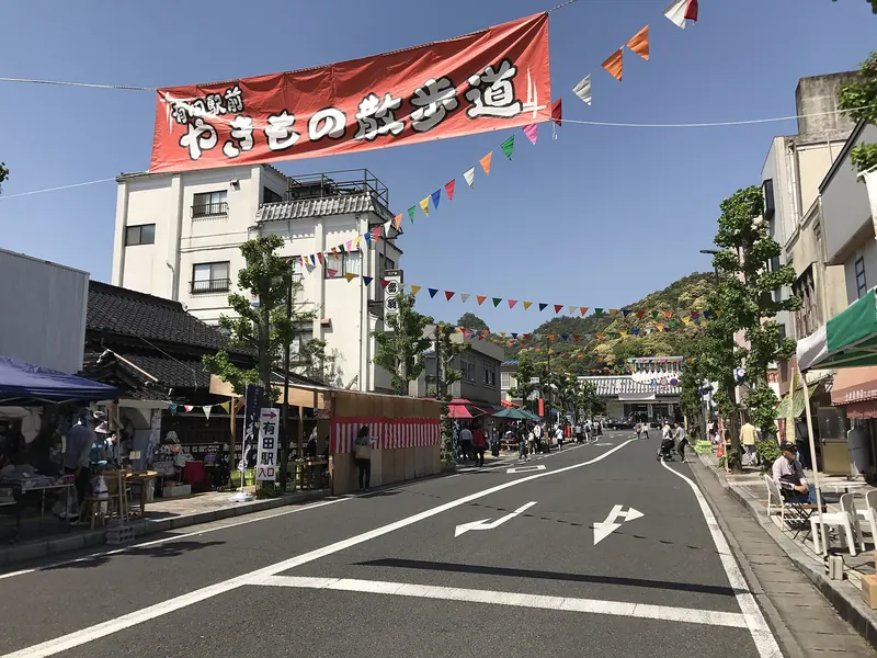A street with a red banner and bunting overhead, stalls on the left and a few visitors in the distance