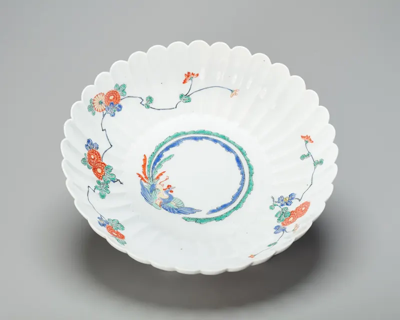 A white porcelain bowl shaped like a flower with scalloped edges, painted with red, blue and green flowers
