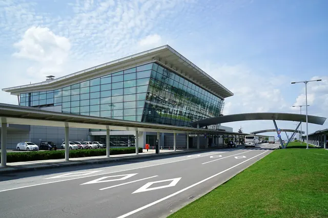 Glass-fronted airport terminal with a covered walkway, the approach road and a lawn