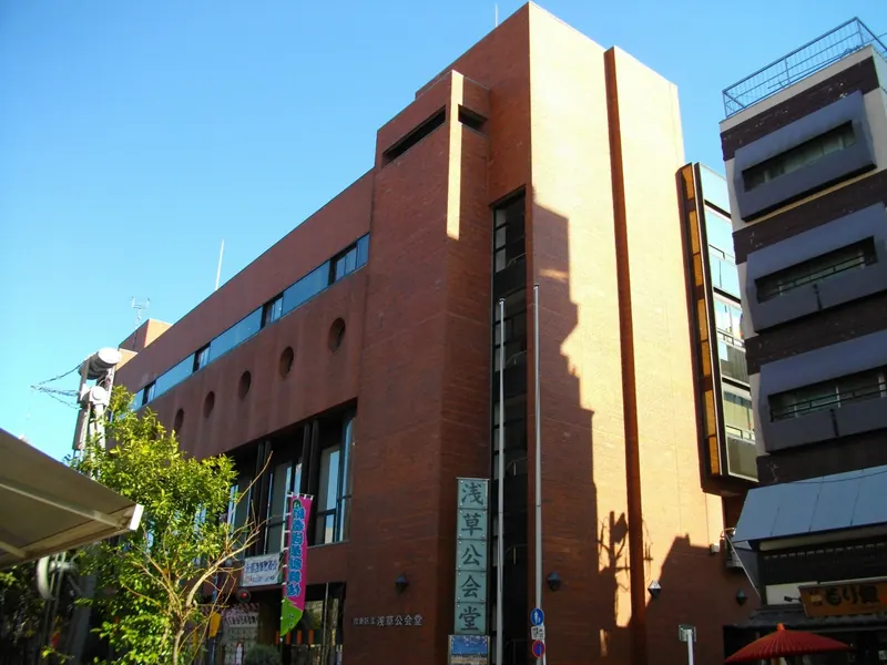 The brown brick Asakusa Public Hall against a blue sky, with a tall vertical sign at its corner