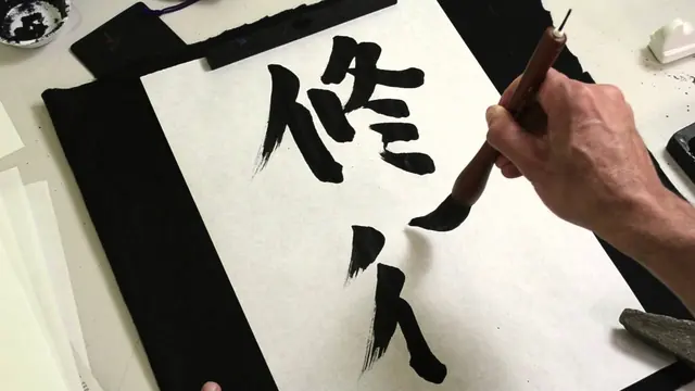 A hand with a brush writing large black characters on white paper