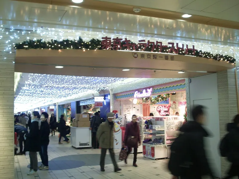 The entrance to Tokyo Character Street with red lettering, Christmas decorations and white lights, and shoppers walking past