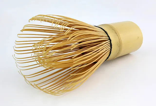 A bamboo tea whisk with many fine curved tines, lying on its side on a white background