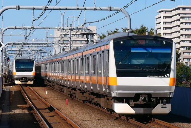 Two silver trains with orange stripes passing each other on the tracks, with apartment blocks behind