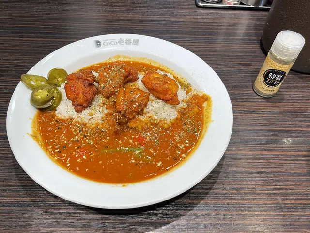 A plate of rice with orange curry sauce, fried chicken and green chillies