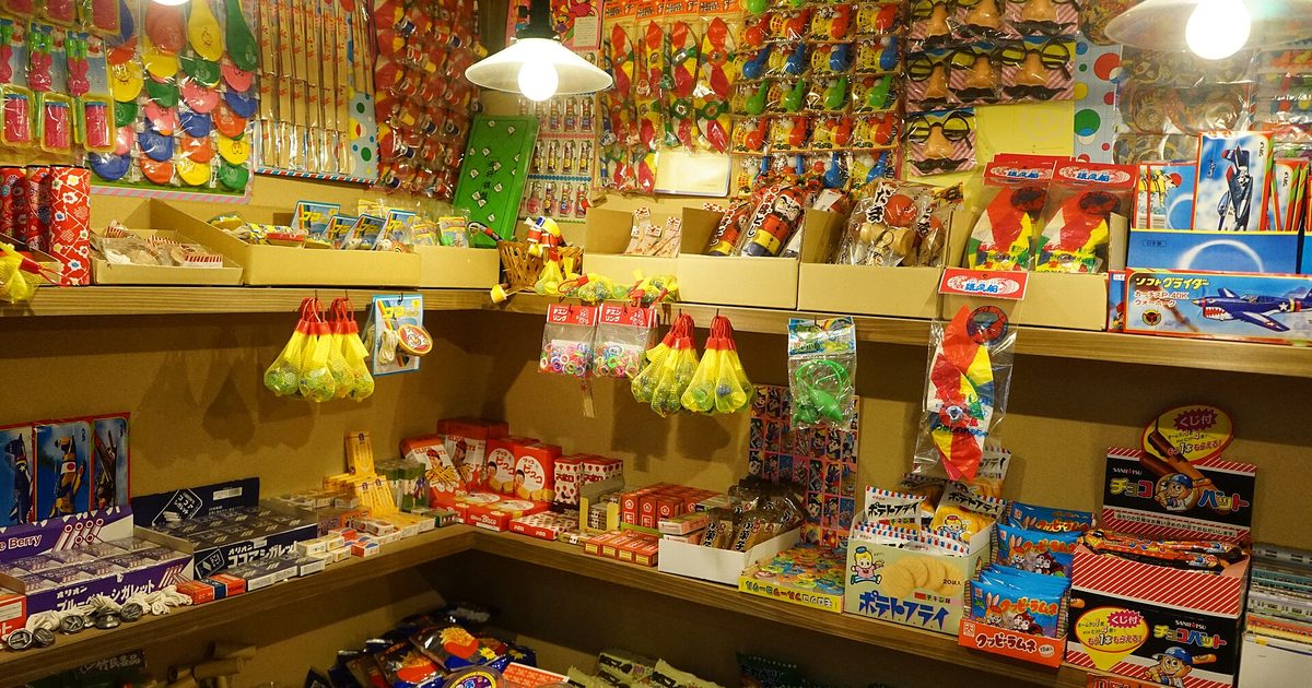 Wooden shelves packed with brightly coloured packets of cheap sweets and small toys under two hanging lamps