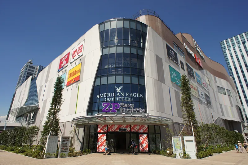 A large white shopping building with a rounded glass corner and a Zepp DiverCity sign over the entrance, under a blue sky
