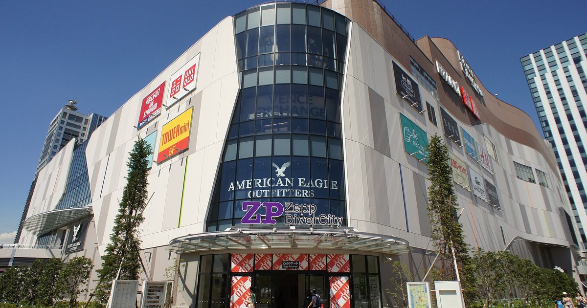 A large white shopping building with a rounded glass corner and a Zepp DiverCity sign over the entrance, under a blue sky