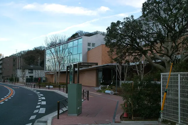 A low building of glass and brick-coloured walls beside a curving road, with a large tree on the right