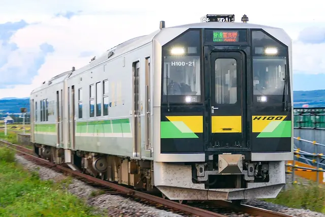 Silver diesel train with green and yellow stripes, its destination display reading Local Furano