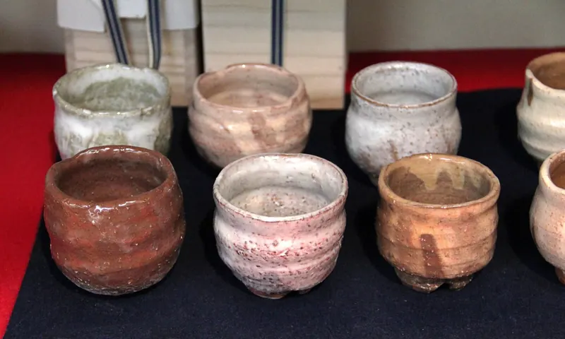 Rows of small cups in pale pink, white and orange-brown glazes on a black cloth