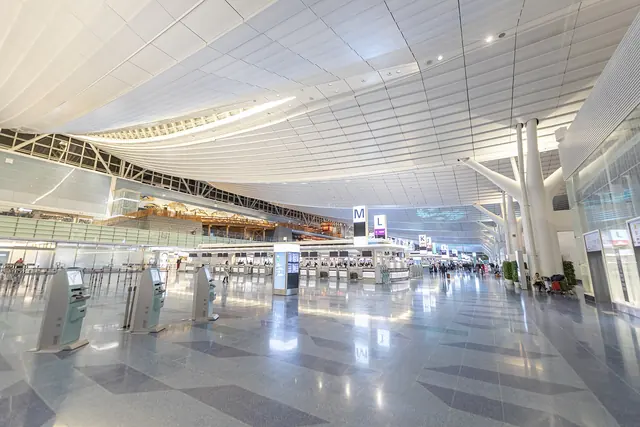 A wide white departure hall with a curved ceiling, check-in counters and a shiny floor