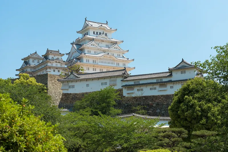 The white keep of Himeji Castle above green trees under a blue sky