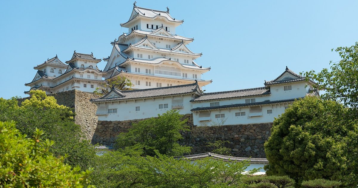 The white keep of Himeji Castle above green trees under a blue sky