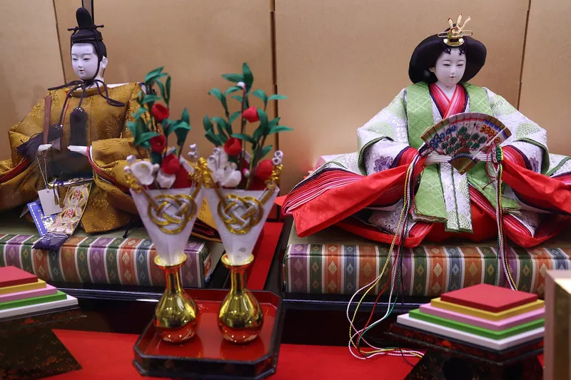 Emperor and empress hina dolls in court dress on a stand with gold screens and flower ornaments