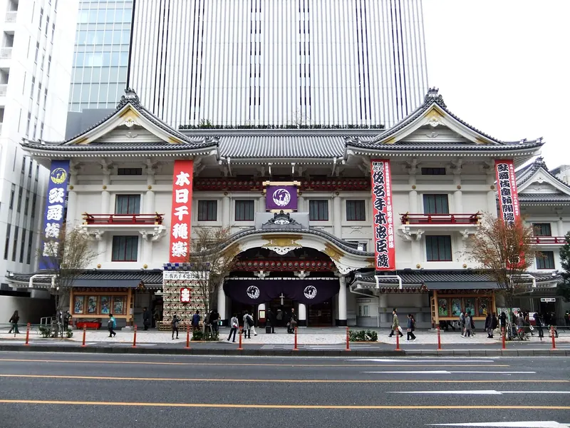 The white front of the Kabuki-za theatre with curved gables and red and purple banners, with a glass tower behind