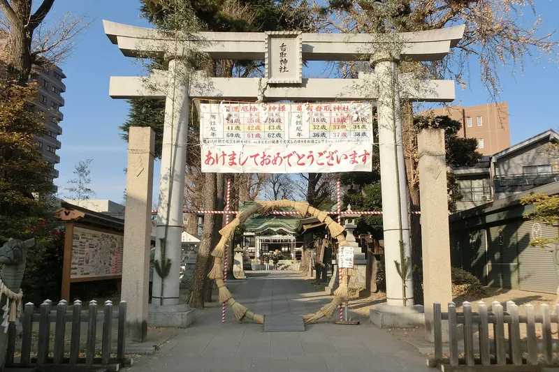 A stone torii gate at the entrance to a shrine, with a New Year banner hung across it and a paved approach leading to a large ring of woven grass
