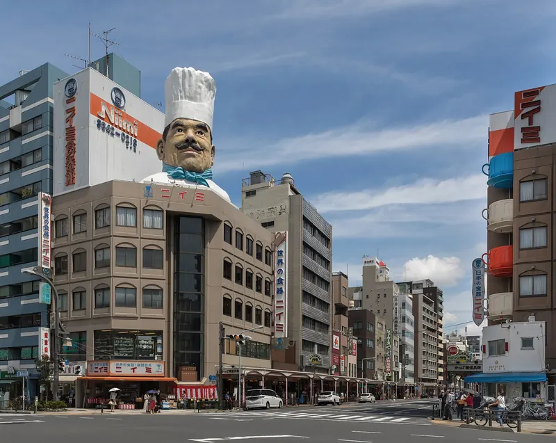 A corner building topped by a giant chef's head in a white hat at a street junction under a blue sky