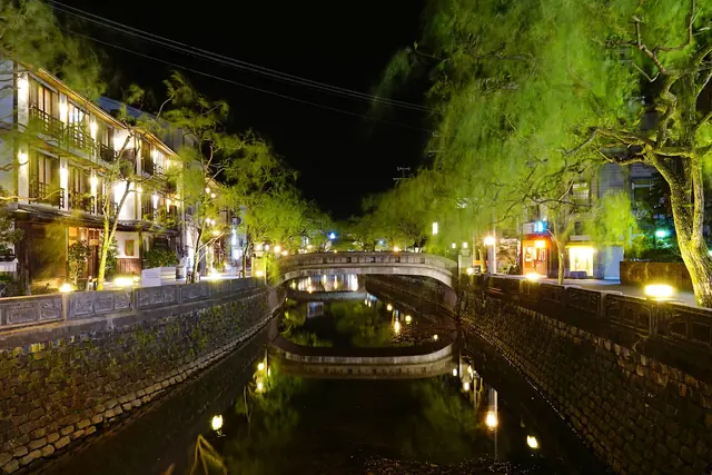 A willow-lined canal at night with lit inns and a stone bridge