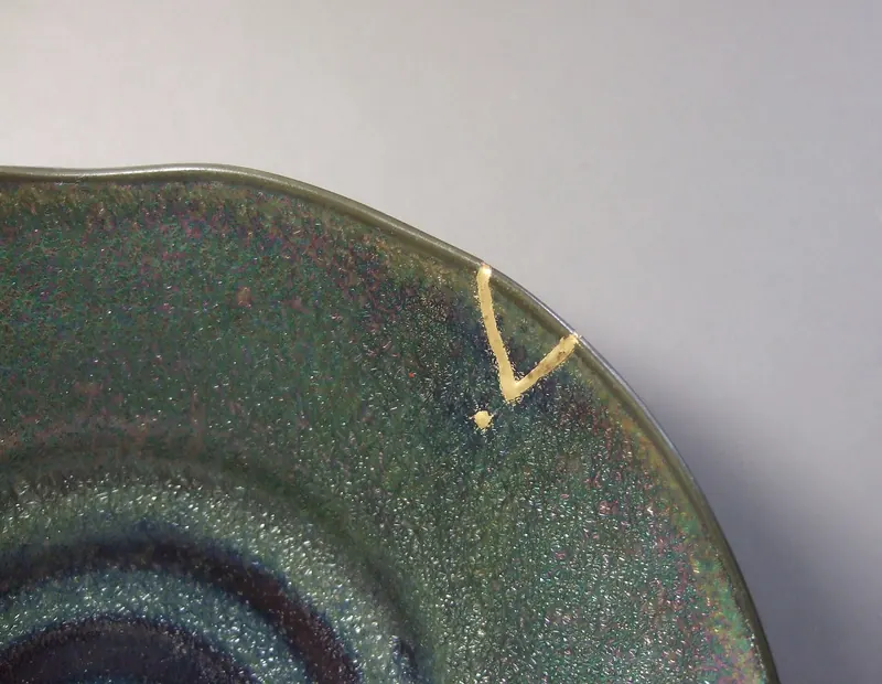 The rim of a green and purple glazed dish with a small V-shaped chip filled with gold