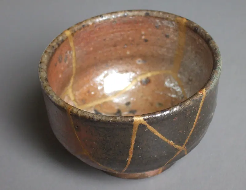 A small brown stoneware cup with thin gold lines running across its cracks