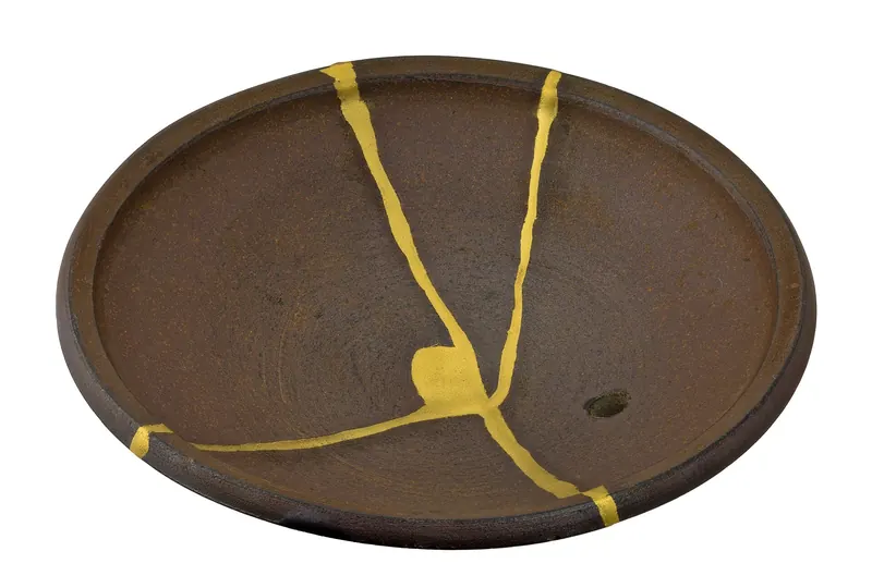 The brown underside of a teapot lid with gold lines joining the broken pieces