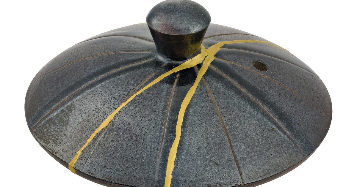 A dark grey teapot lid with a knob on top, its cracks joined by bright gold lines