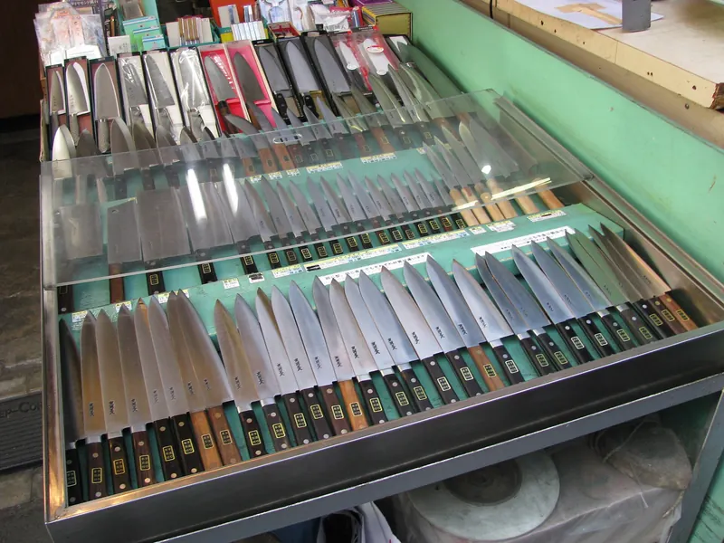 A glass display case with rows of kitchen knives