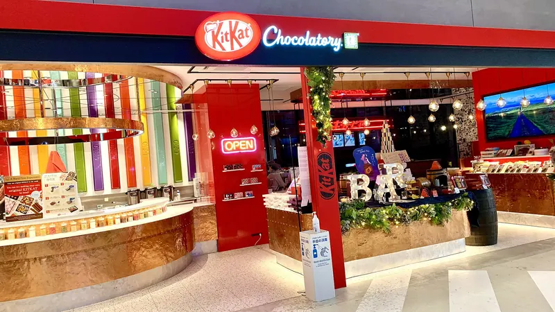A shop front with a red Kit Kat Chocolatory sign, rainbow-striped columns and counters of boxed chocolates