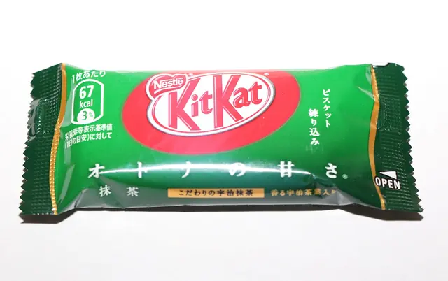 A mini Kit Kat in a green wrapper printed in Japanese, lying on a white background