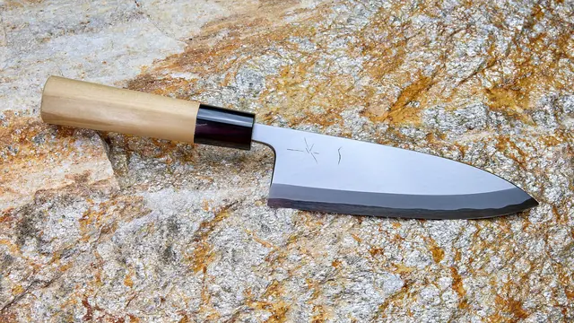 A thick, wide deba knife with a pale wooden handle, lying on a rock