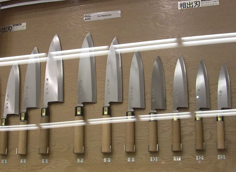 A row of deba knives in graded sizes hanging on a wall, each with a numbered tag