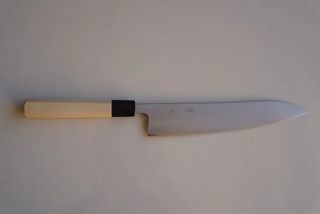 A long, pointed Japanese chef's knife with a plain steel blade and a pale wooden handle, on a grey background