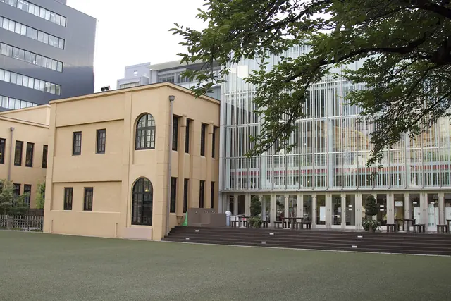 A cream two-storey former school building and a glass wing behind a lawn of artificial turf