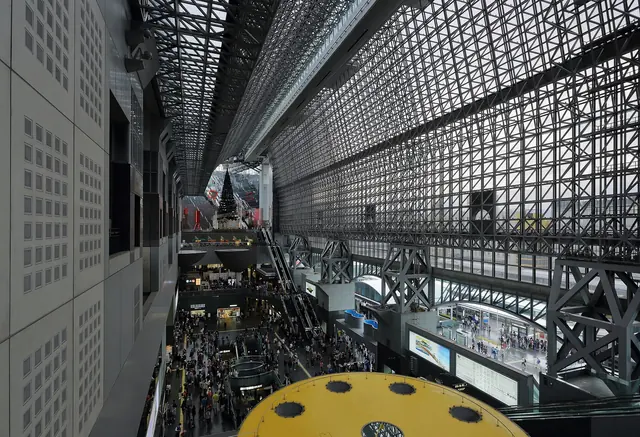 The steel-and-glass atrium roof of Kyoto Station seen from a high level with people small on the concourse below