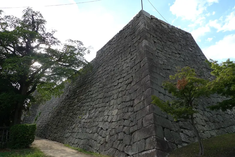 A tall curved stone wall of Marugame Castle between trees