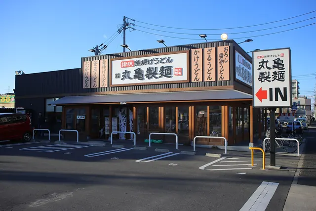 A Marugame Seimen udon restaurant with wooden signs along the roof and a car park in front