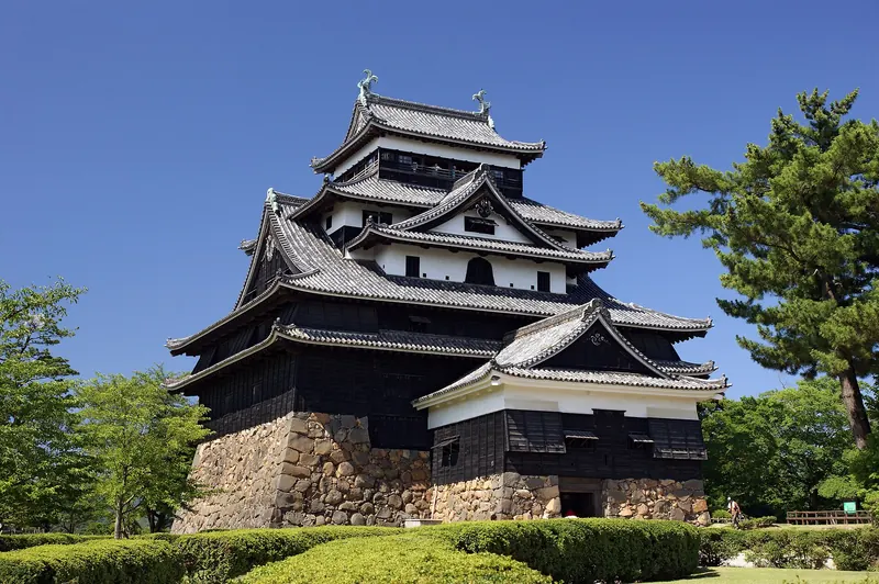 The black wooden keep of Matsue Castle on its stone base under a blue sky