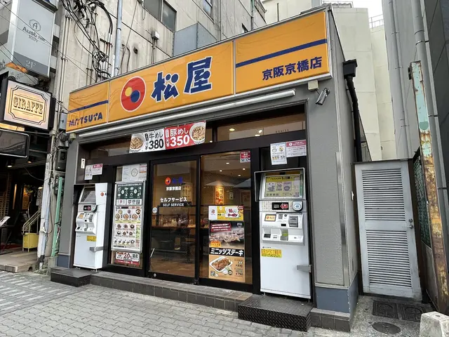 The front of a Matsuya restaurant with an orange sign and meal-ticket machines on both sides of the door