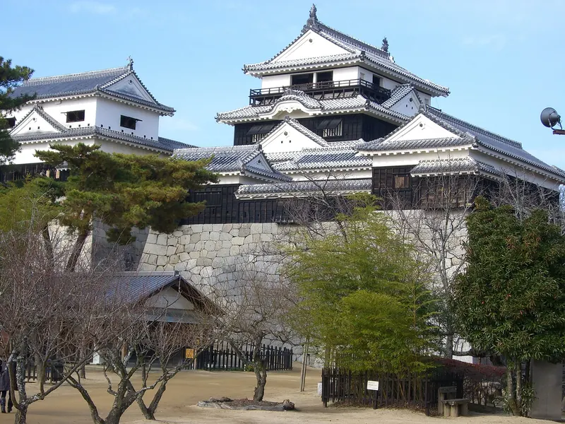 The white keep and towers of Matsuyama Castle on high stone walls in winter