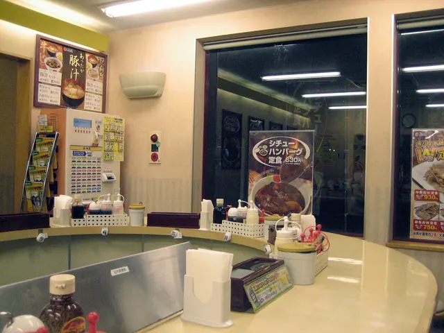 Counter seats with condiments in a small restaurant and a meal-ticket machine against the wall on the left