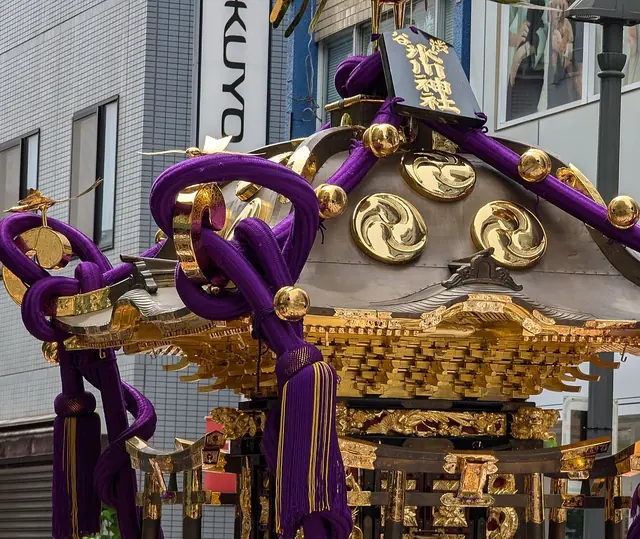 A black-and-gold portable shrine with thick purple cords and gold ornaments in a city street