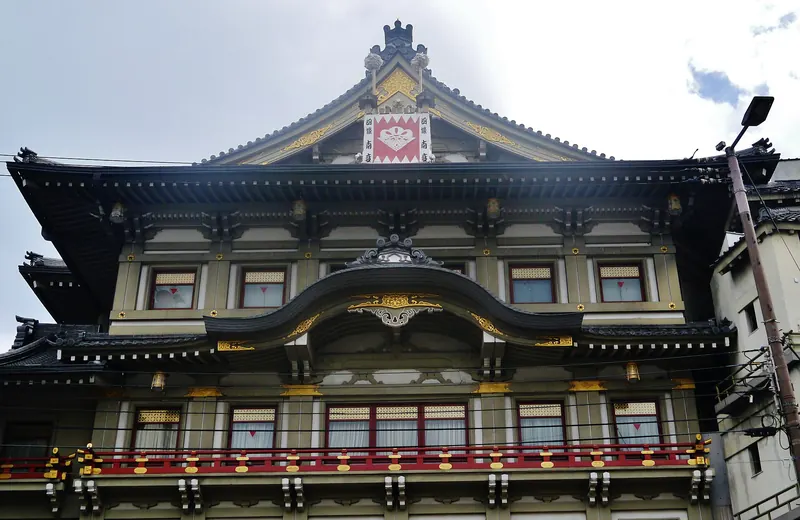 The ornate front of the Minamiza theatre in Kyoto, with layered tiled roofs, a crest on the gable and a red railing along the balcony