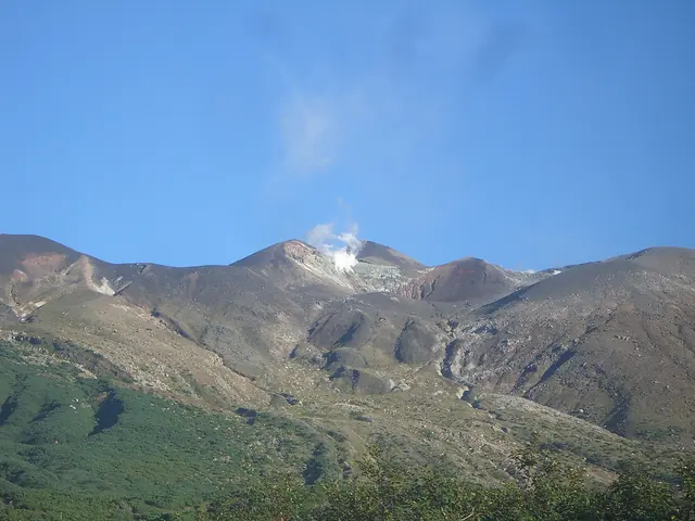 Volcano with a white plume of steam rising from its crater under a blue sky