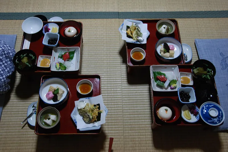 Red lacquer trays of small vegetarian dishes, with tempura, tofu and pickles, laid out on tatami