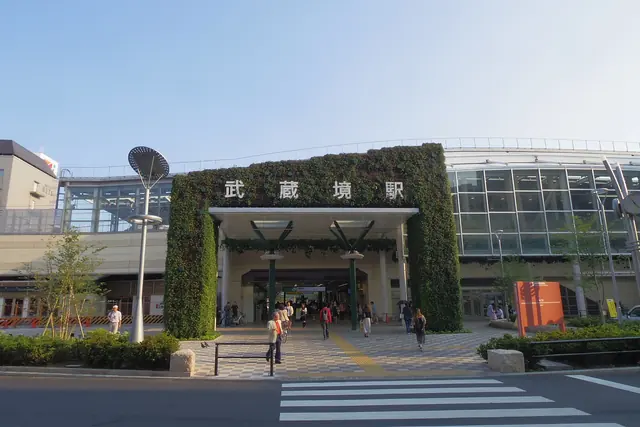 A station entrance below a green wall carrying the station name in Japanese, seen across a pedestrian crossing
