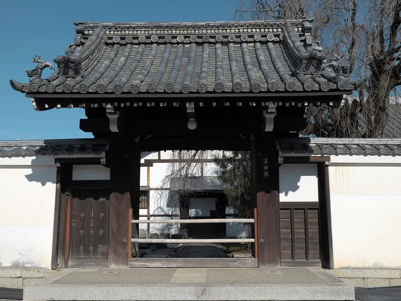 A dark wooden temple gate with a tiled roof set in a white wall