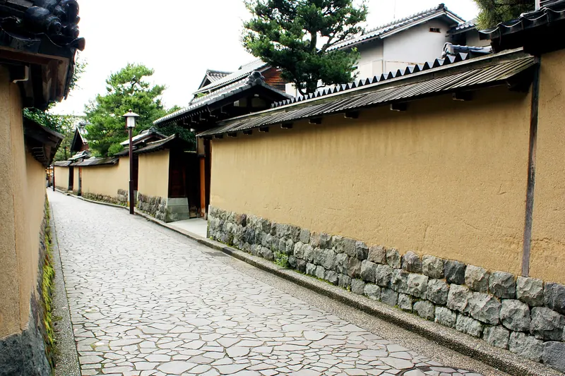 A stone-paved lane between ochre earthen walls with tiled tops and stone bases in Kanazawa